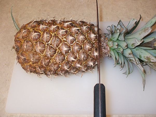 cutting the top off a whole pineapple